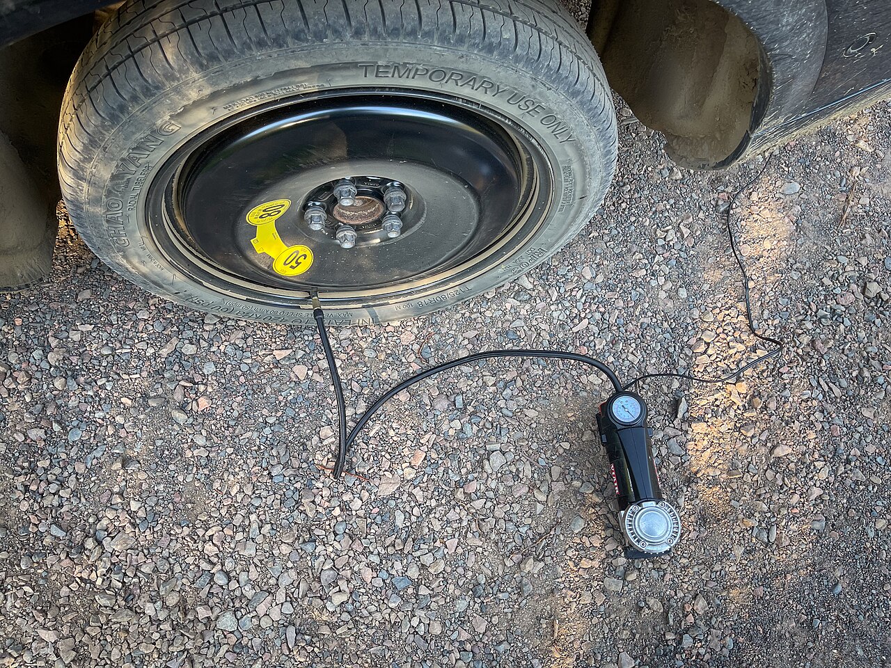 Portable tire inflator connected to a temporary spare tire beside a vehicle