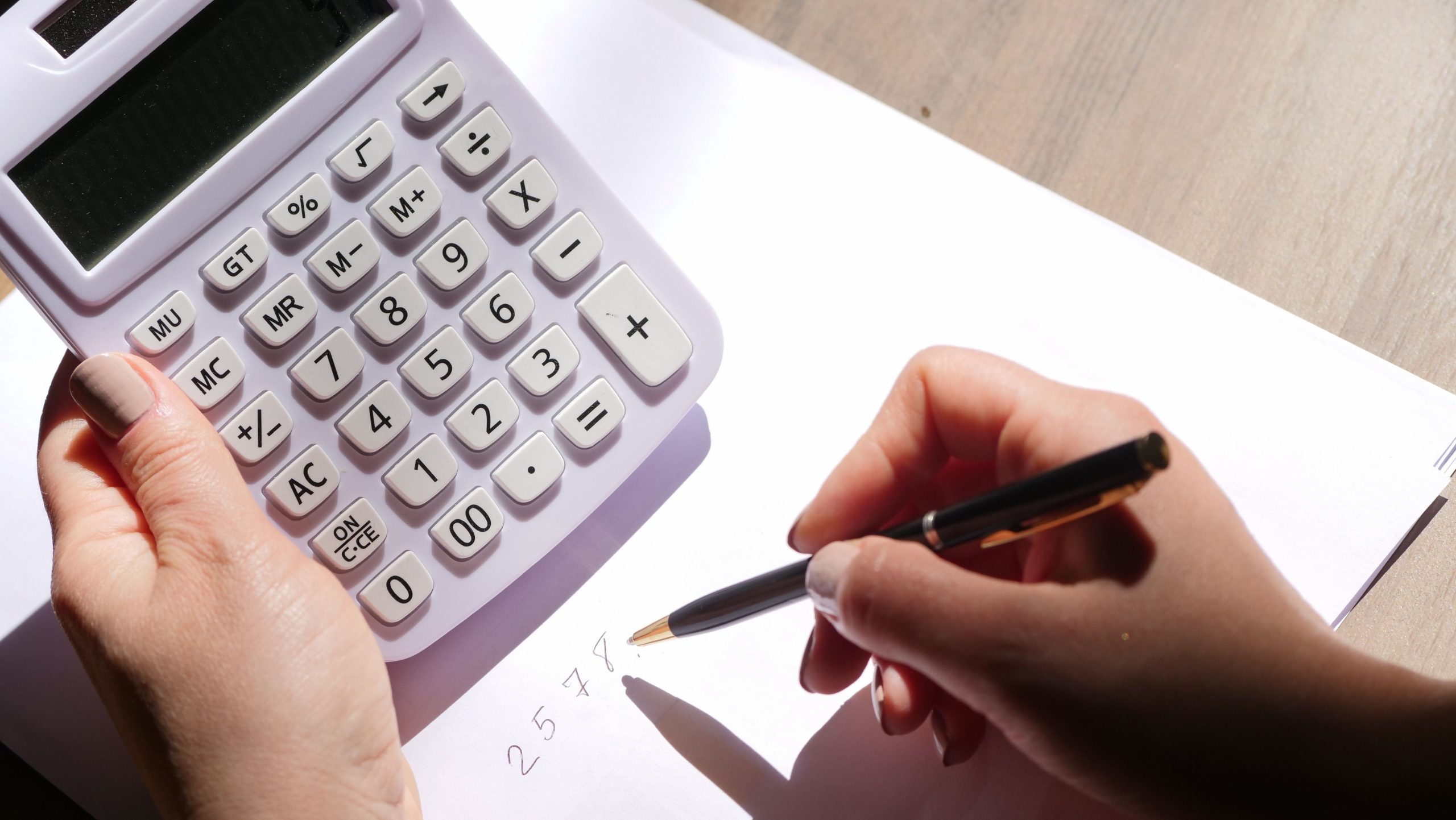 Person using a calculator and pen while working through calculations at a desk